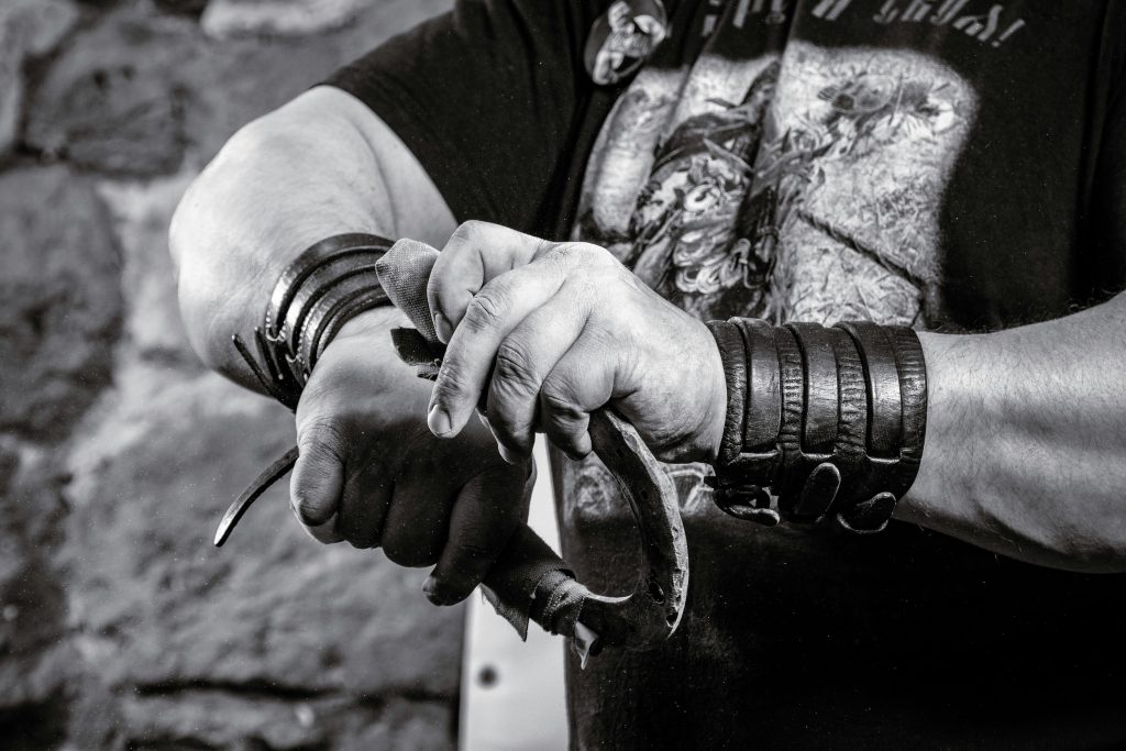 Black and white photo focusing on hands wearing leather bracelets, gripping a tool.